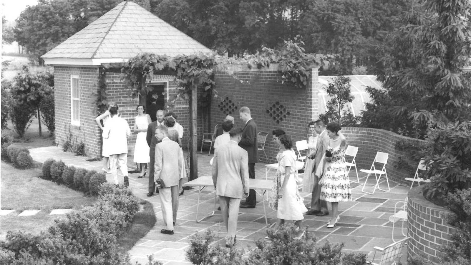 A black and white image with a group of people gathers around a brick patio and teahouse