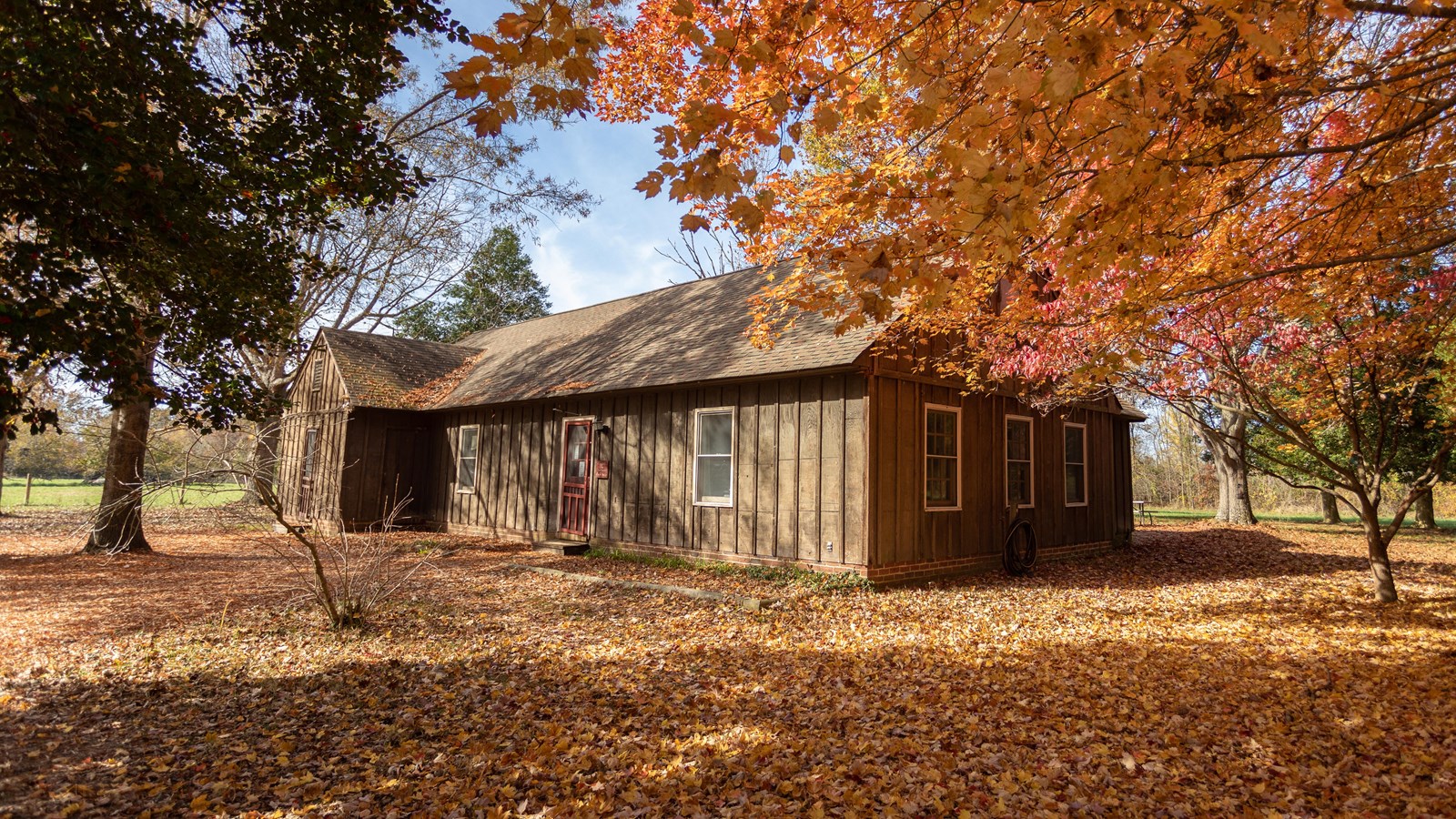 A one story building with dark brown wooden siding and a red door.