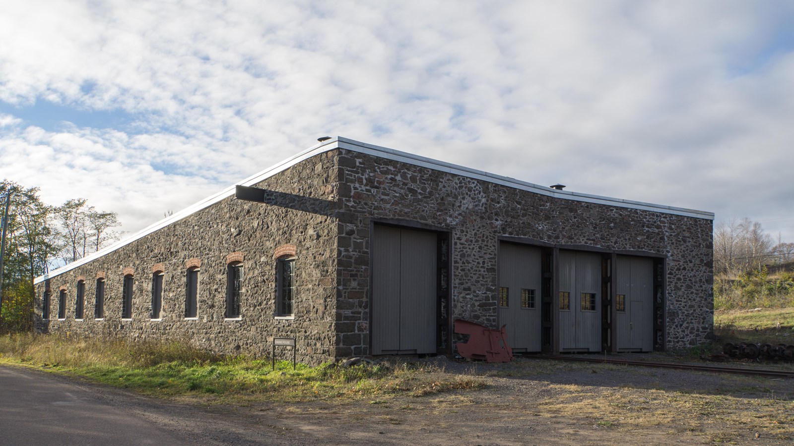 Rectangular stone building with a flat sloped roof and window openings along the side and four doors