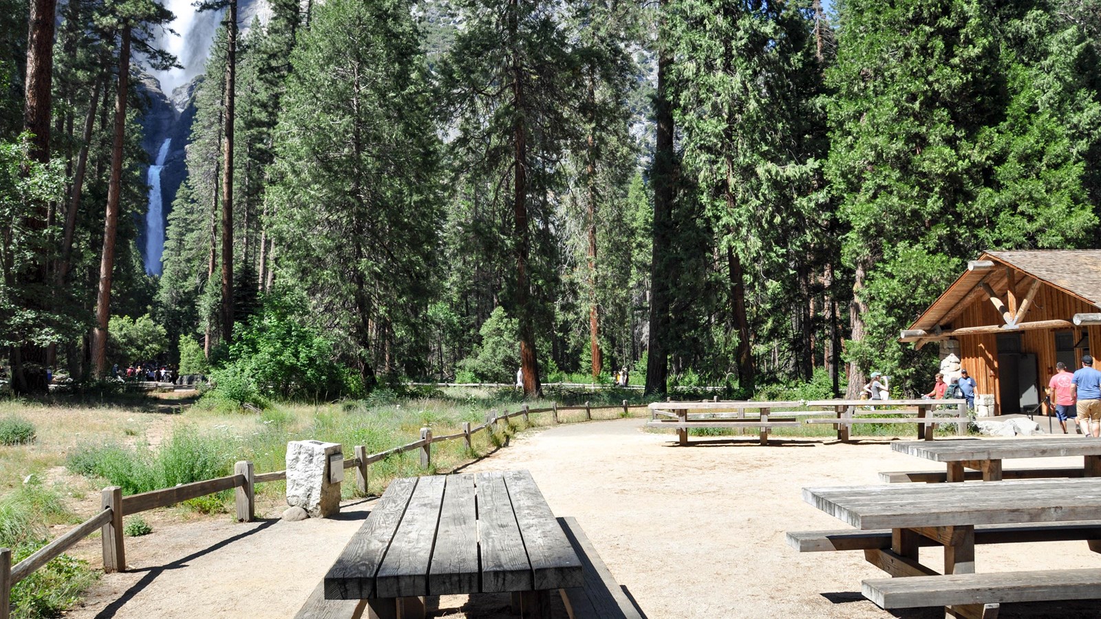 Wooden picnic tables, restroom building and waterfall in background
