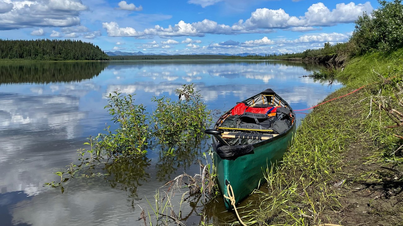 A green pack canoe is tied to the bank of the broad Kobuk River.