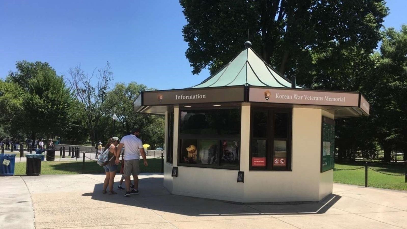 Two people in front of a small, octogonal information kiosk.