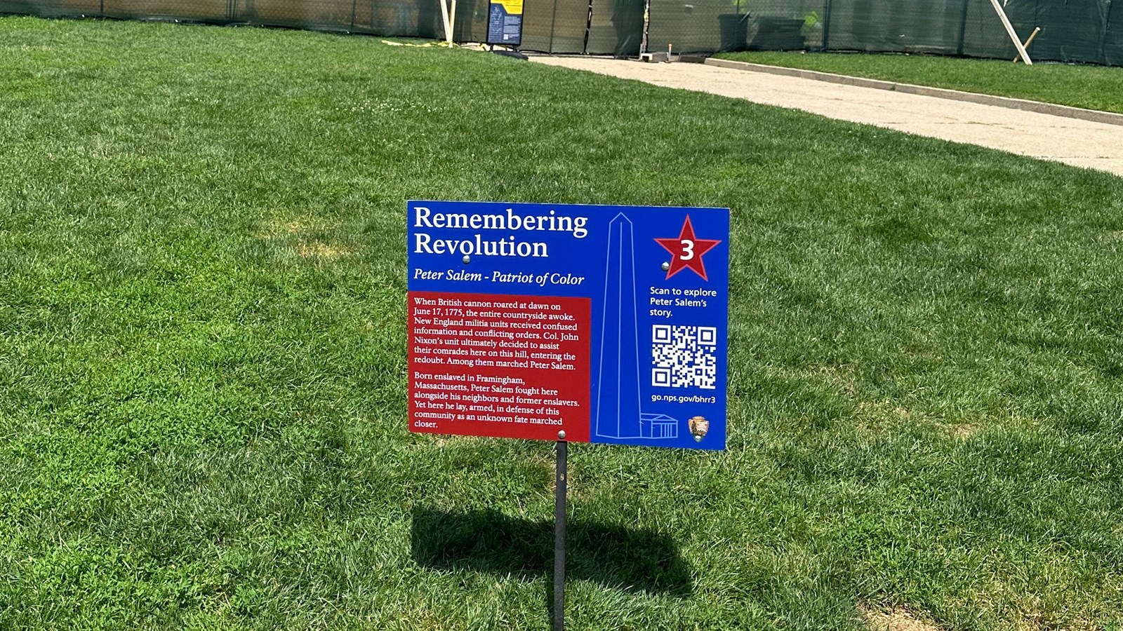 Red and blue wayside next to southeast corner marker on lawn.