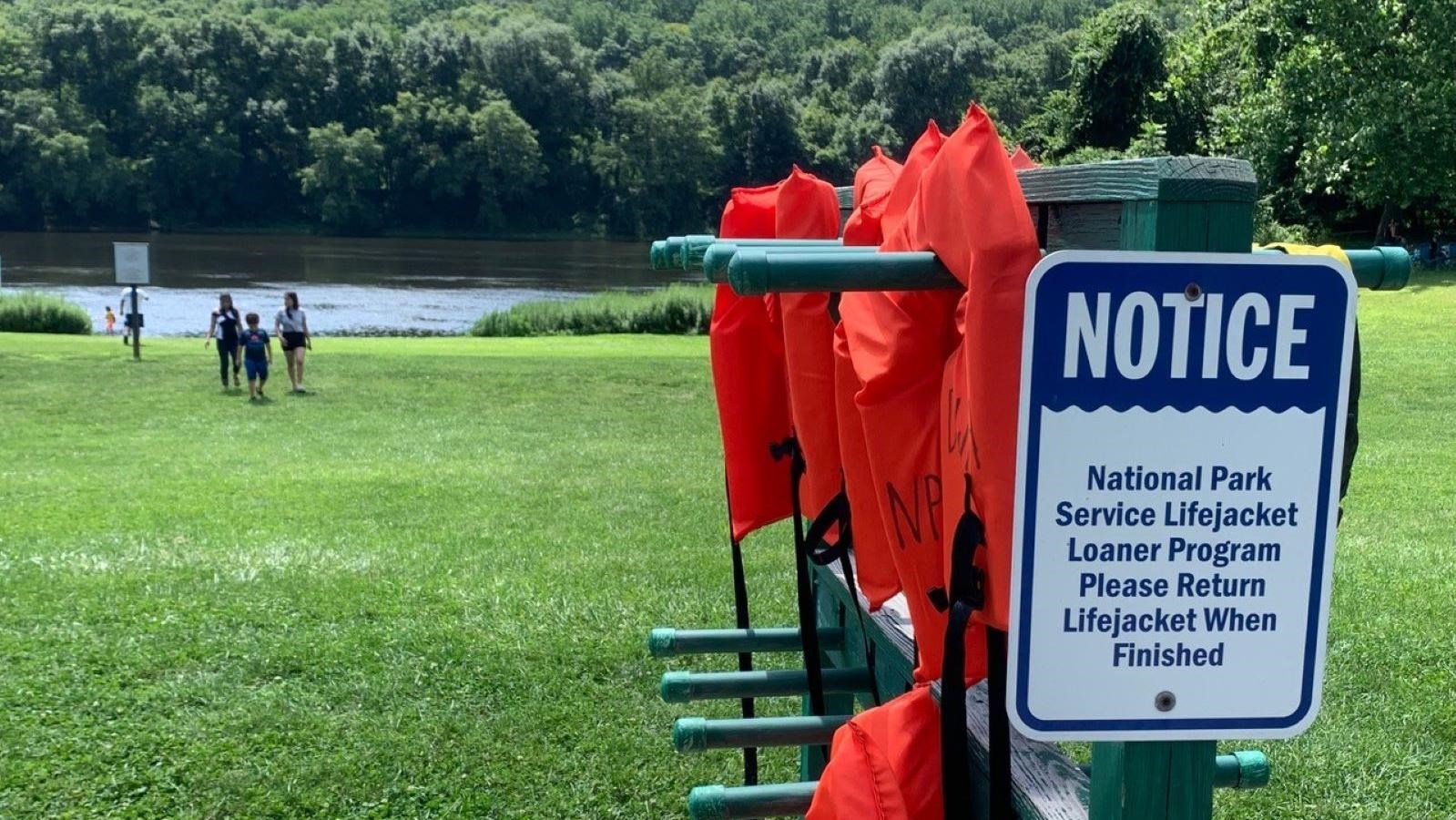 A rack with orange life jackets hanging on them and a sign explaining the NPS loaner program.