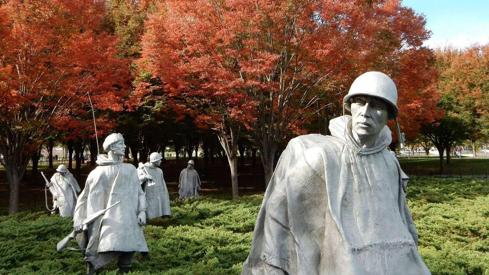 Statues of soldiers in low shrubbery with fall-colored trees in background.