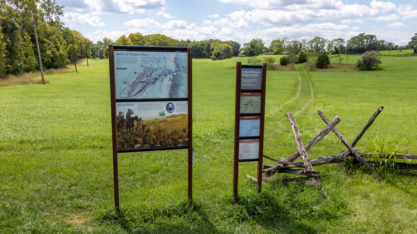 Two vertical information panels at the start of a grass track up a slope.