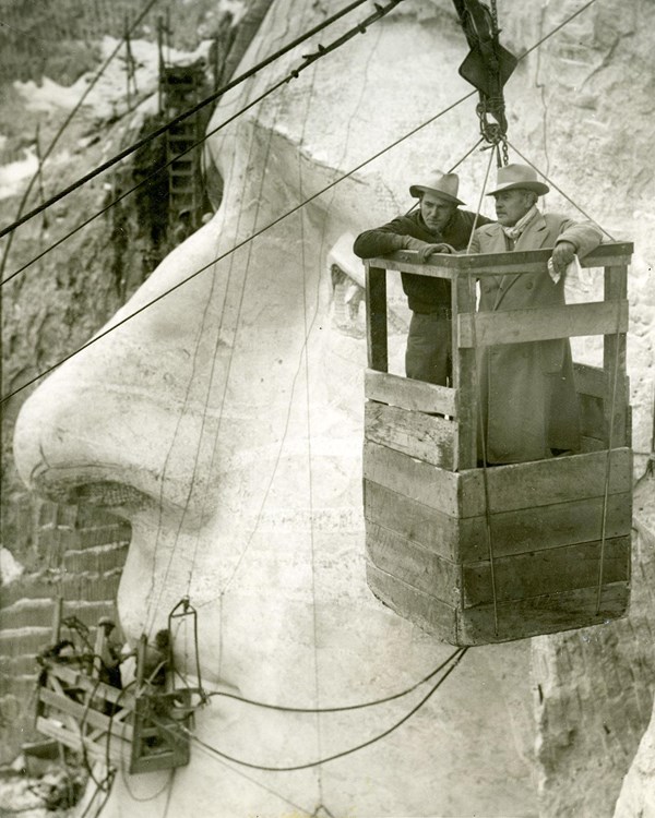 Gutzon Borglum (right) and Lincoln Borglum observing work on Mount Rushmore from the tram car.