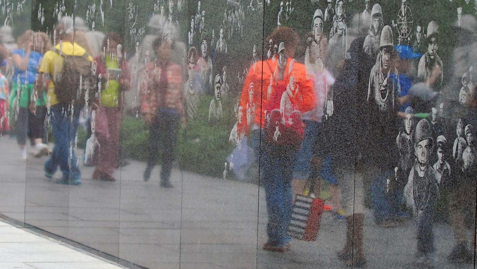 Wall of soldier images reflecting visitors passing by.