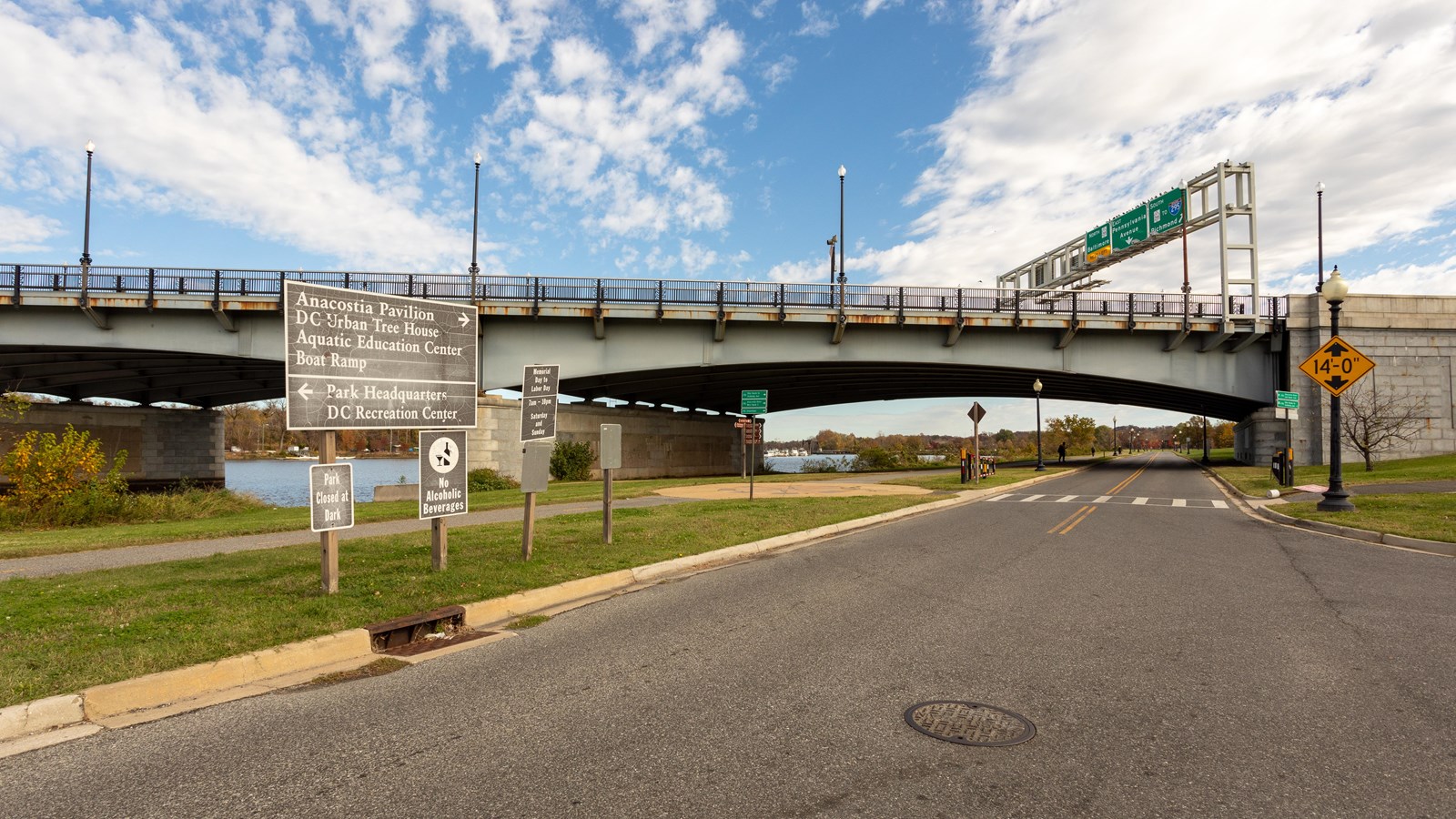 A highway bridge is positioned behind four signs directing location. 