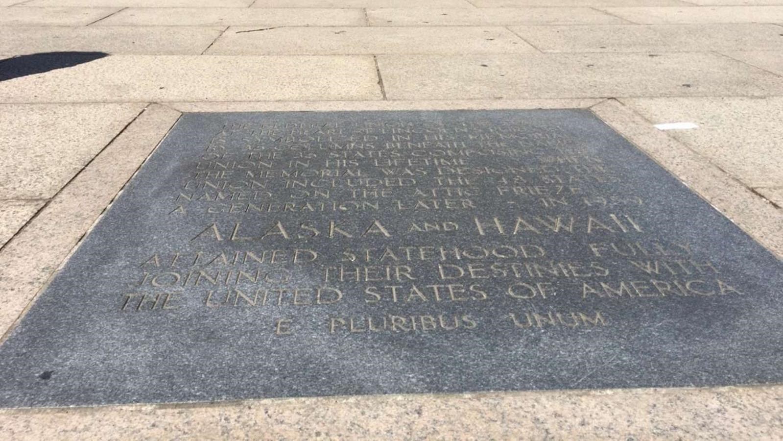Large, rectangular plaque in walkway with visitors in background.