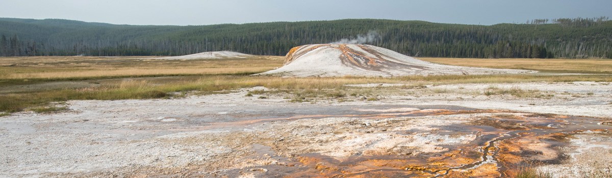 Hydrothermal features steam in the middle of a wide-open field.