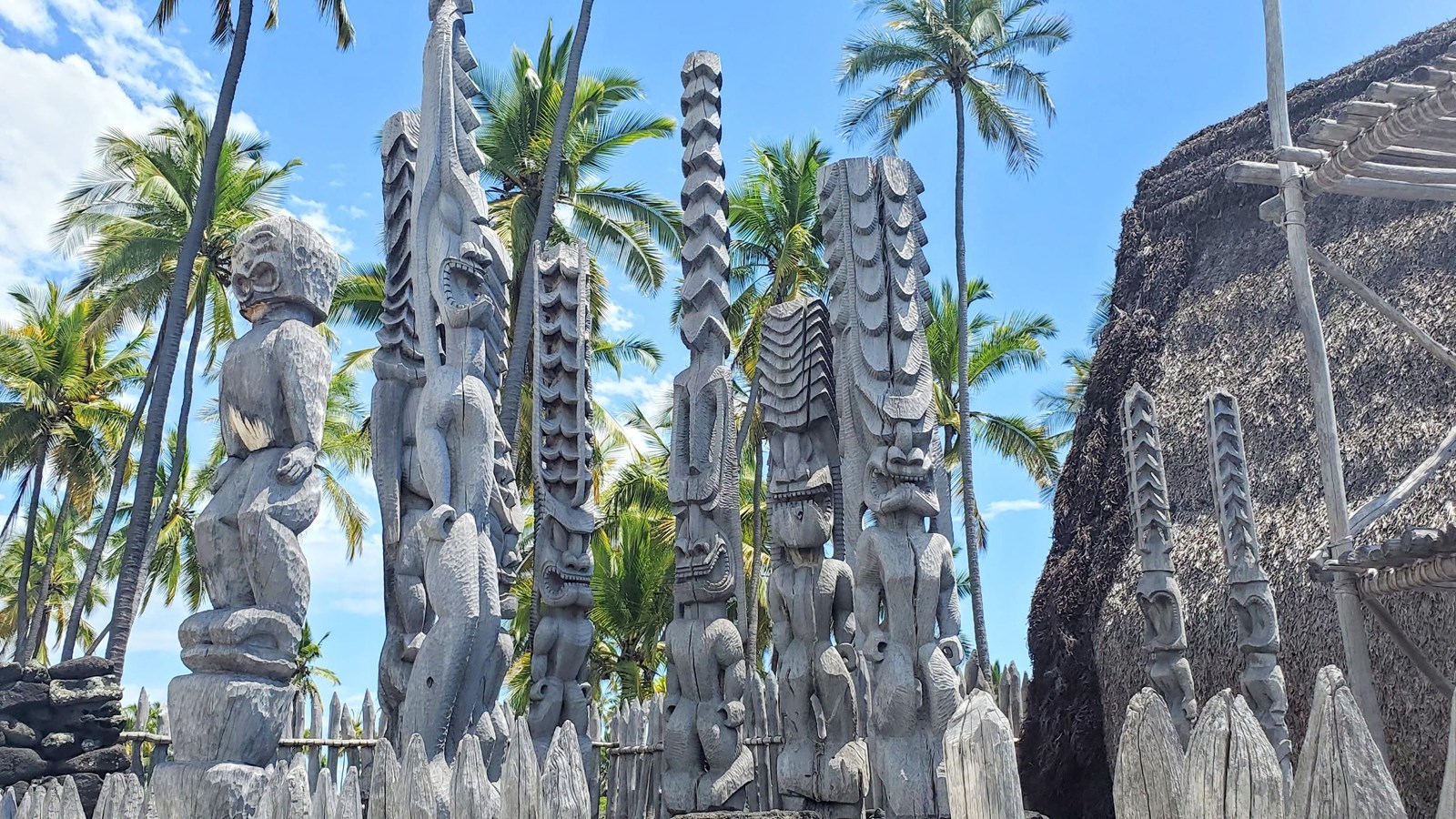 A semi circle of carved kiʻi images stand tall within the wooden palisade of Hale o Keawe
