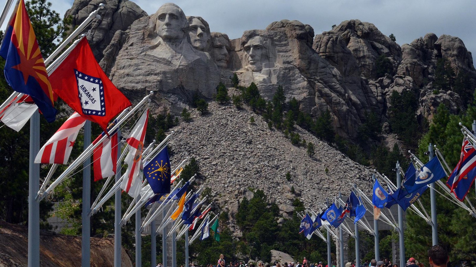 Photo of visitors walking along the Avenue of Flags with Mount Rushmore in the background.