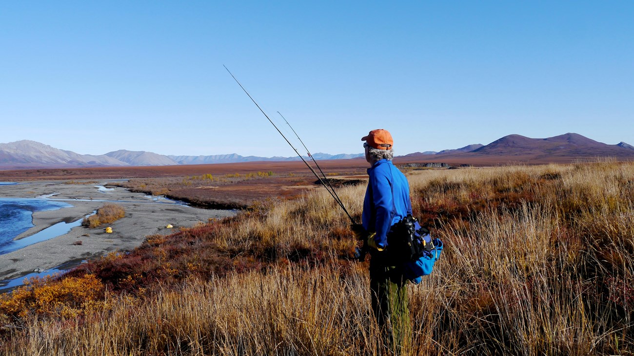 Man standing with fishing pole on tundra, water in the background