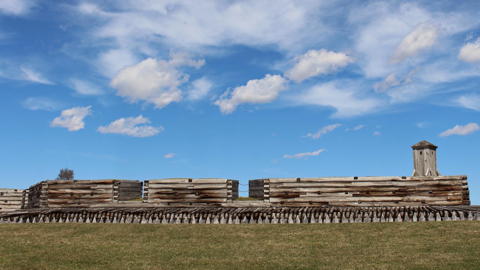A wooden, log cabin style wall stretches out in front of you. A small sentry box sits at the corner.
