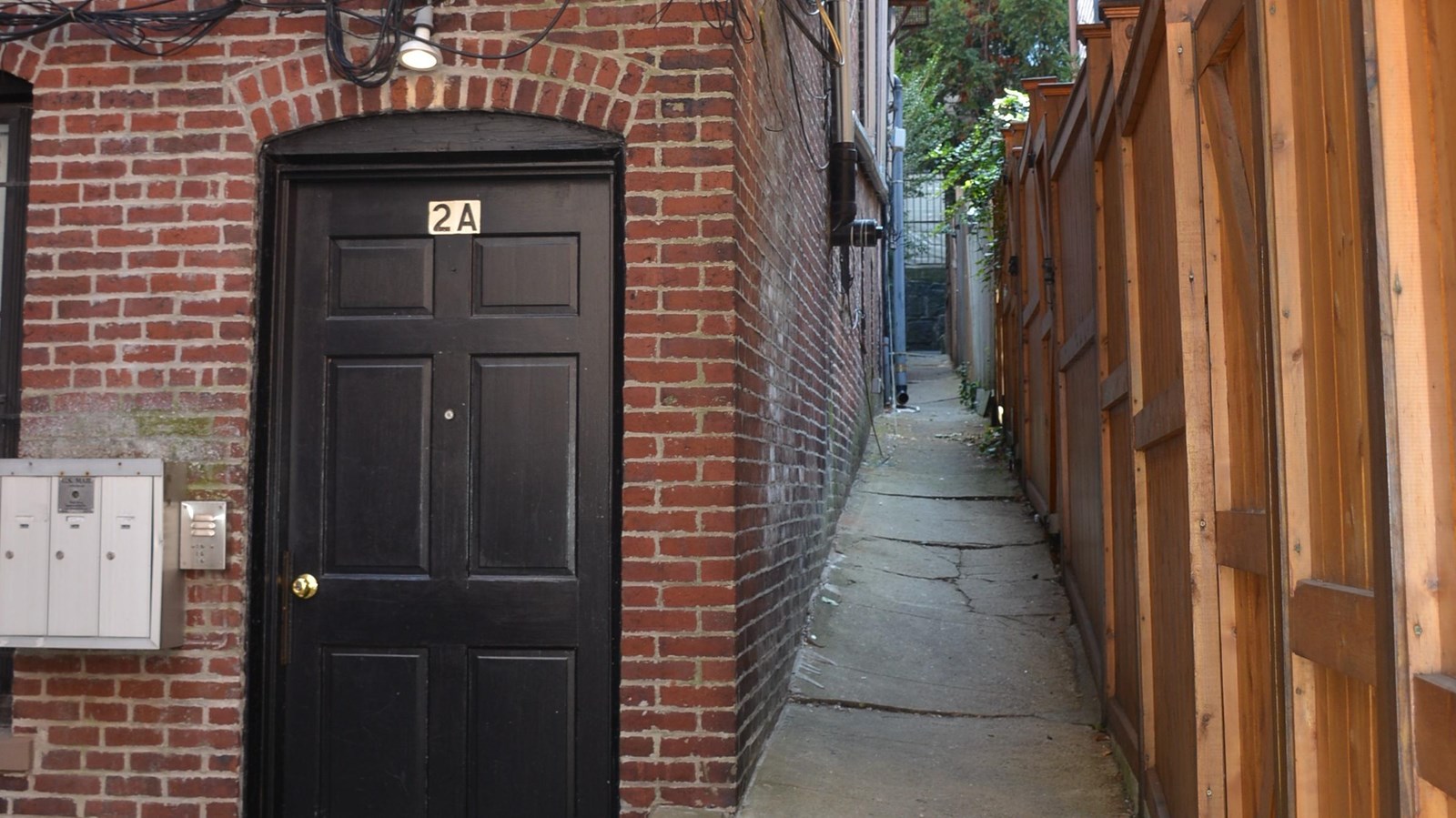 An alley on the right with a brick building on the left with a black door. 