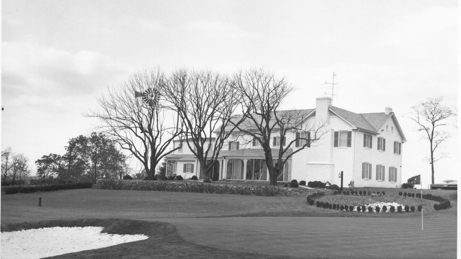 A black and white image of a putting green with an adjacent sand-trap with the white Eisenhower Home