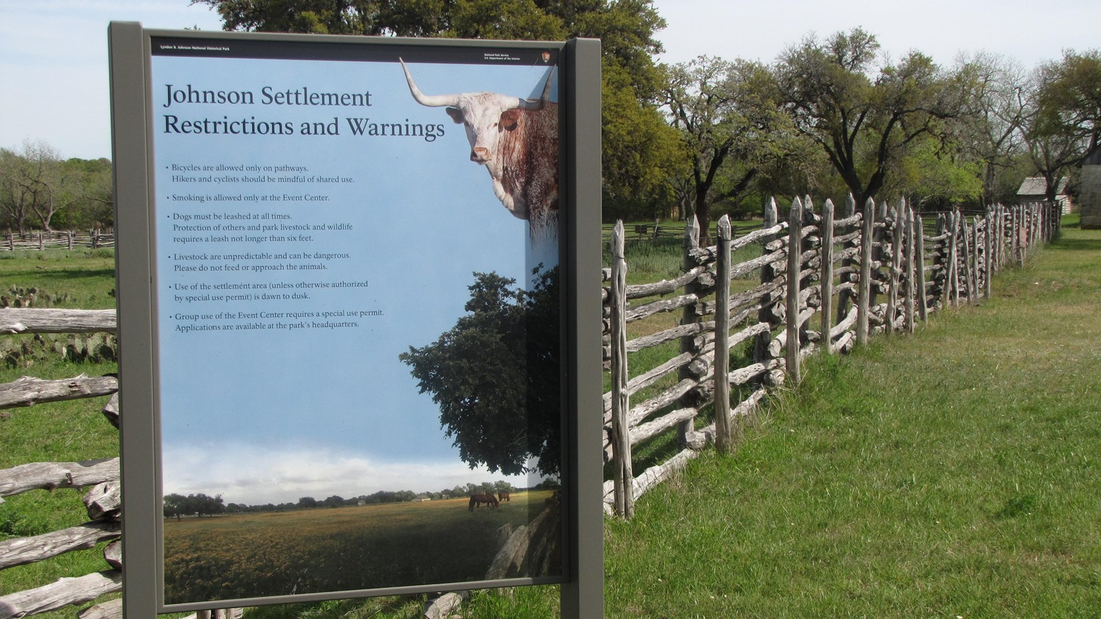 A modern sign stands in front of an old, wooden, pioneer fence.