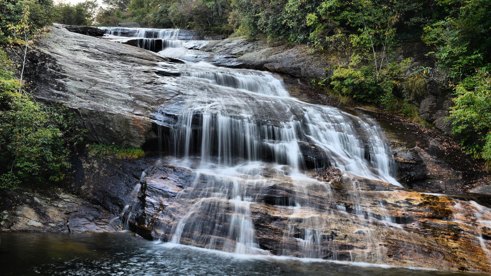 Water flows over tiered rocks into a large pool at the bottom of the waterfall