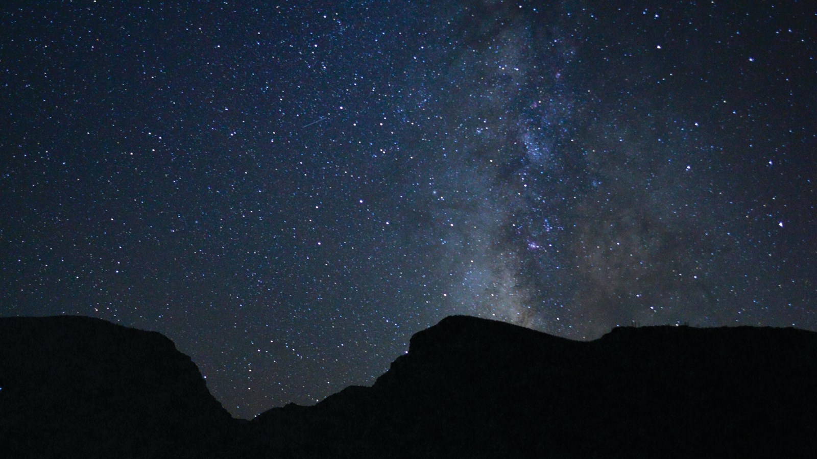 A night sky with the the milky way streaking directly upwards from a vast, deep canyon.