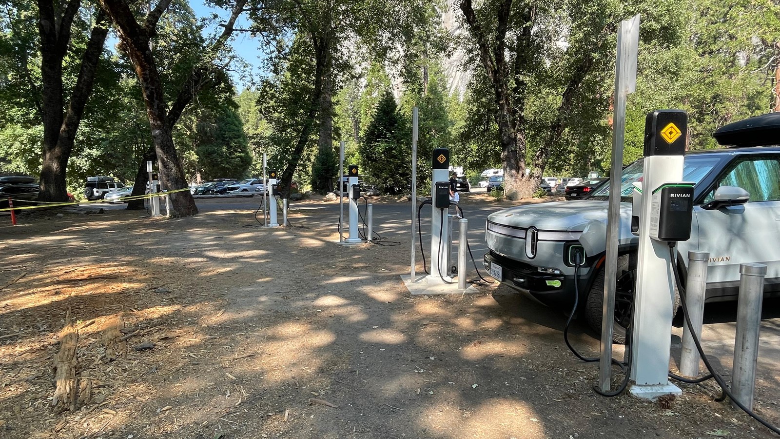 A row of EV charging stations along the edge of a parking lot next to a dirt area
