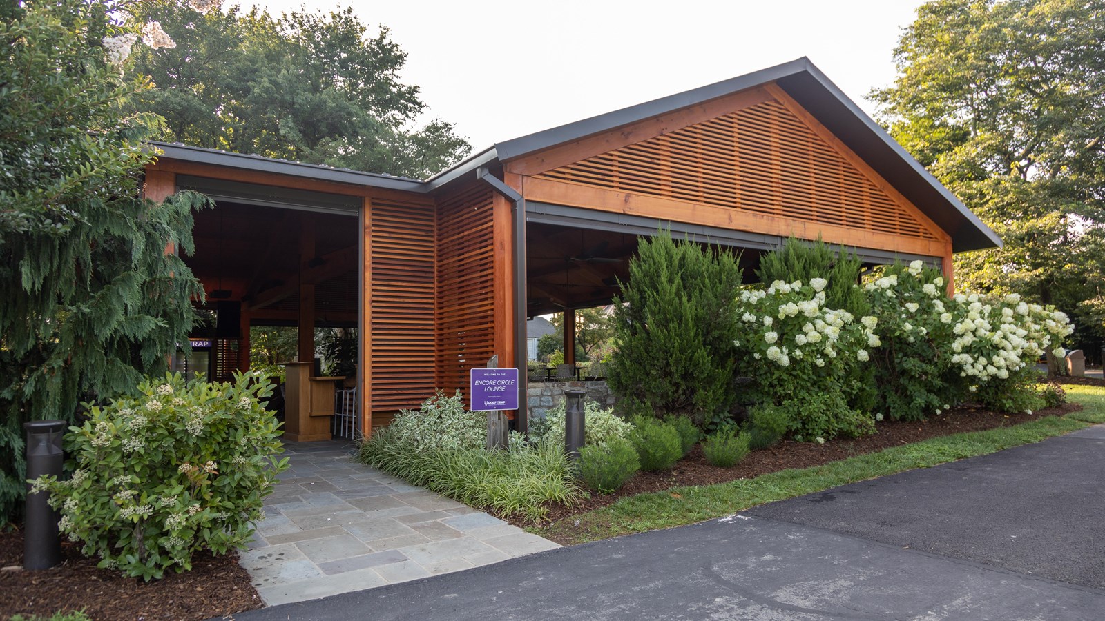 Stone pathway leads into a wooden pavilion with purple sign in front.