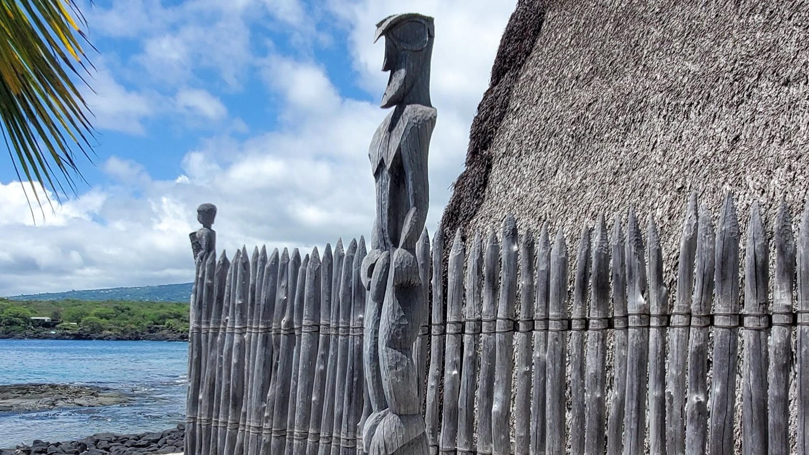 A carved kiʻi (temple image) stands in front of the wooden palisade of Hale o Keawe