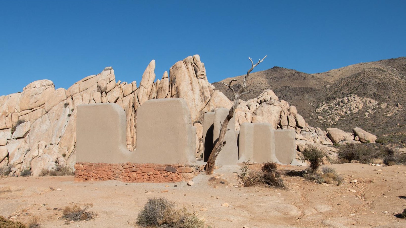 A historic adobe type structure with boulders and a mountain in the background.