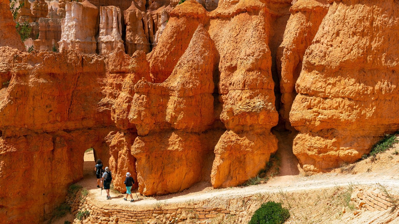 Hikers walk along a trail towards an open archway in the red rock