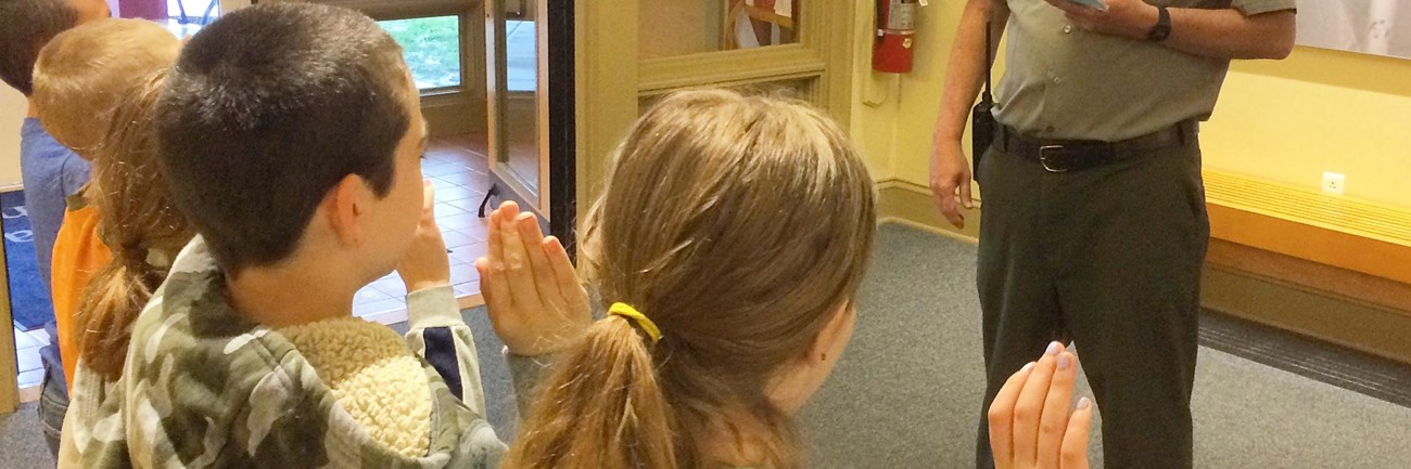 children taking a pledge in the foreground with a Park Ranger standing in the background. 