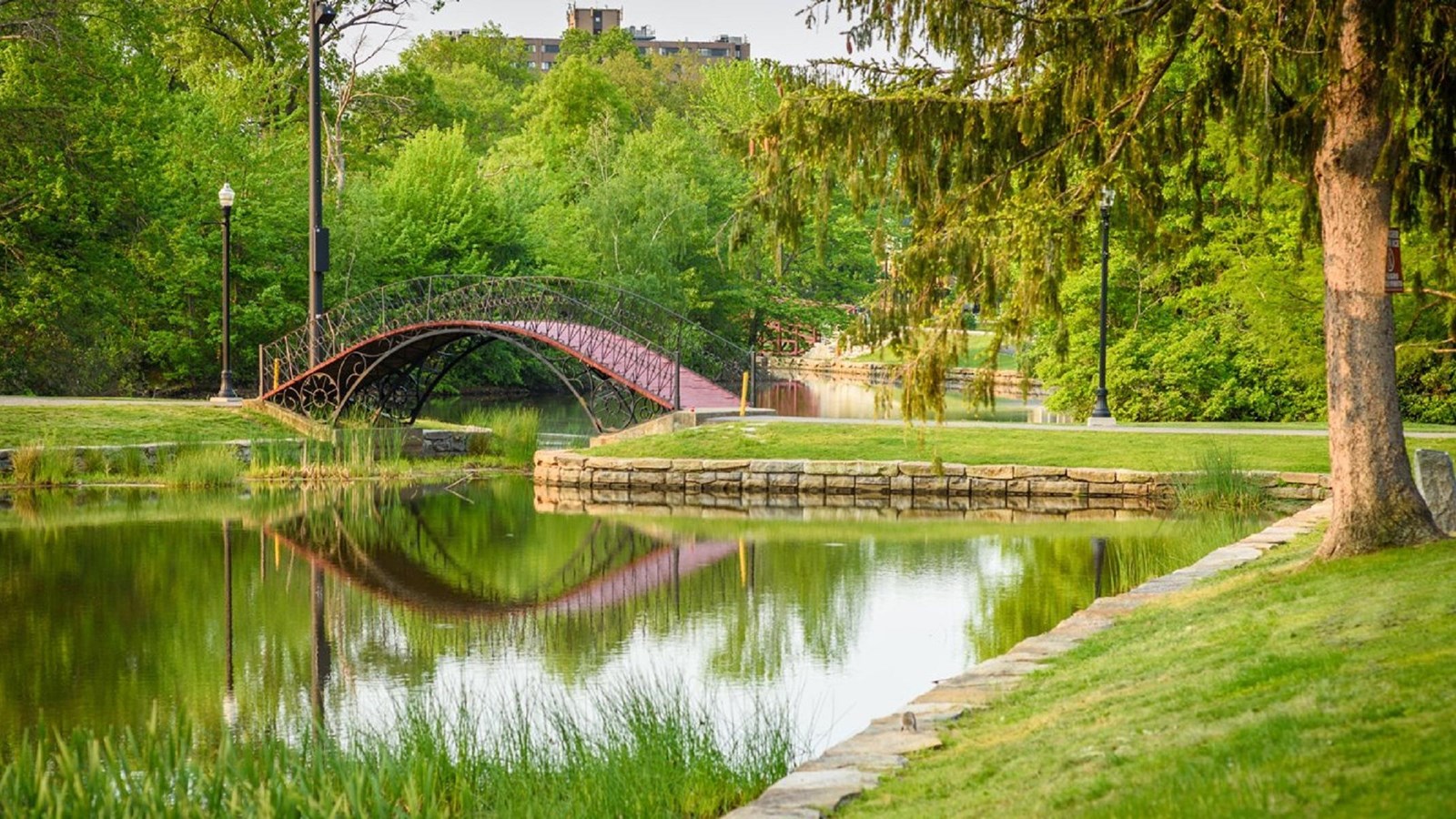 Bridge over water between two grassy areas with trees around them.