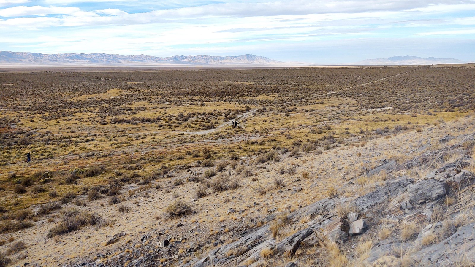Expansive land with rocks, mountains in the foreground, and a path crossing diagonally in the photo.