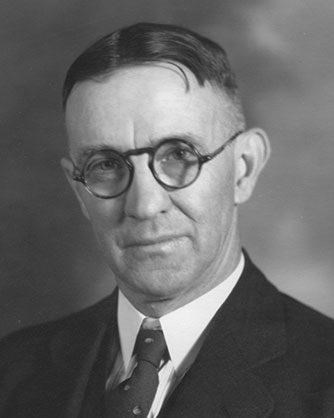 Black and white photographic portrait of a man in a dark suit, tie, and white shirt.
