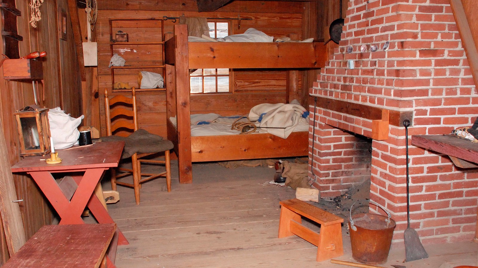 A room with a large fireplace hearth and a bulky wooden bunkbed. Personal items are strewn around it
