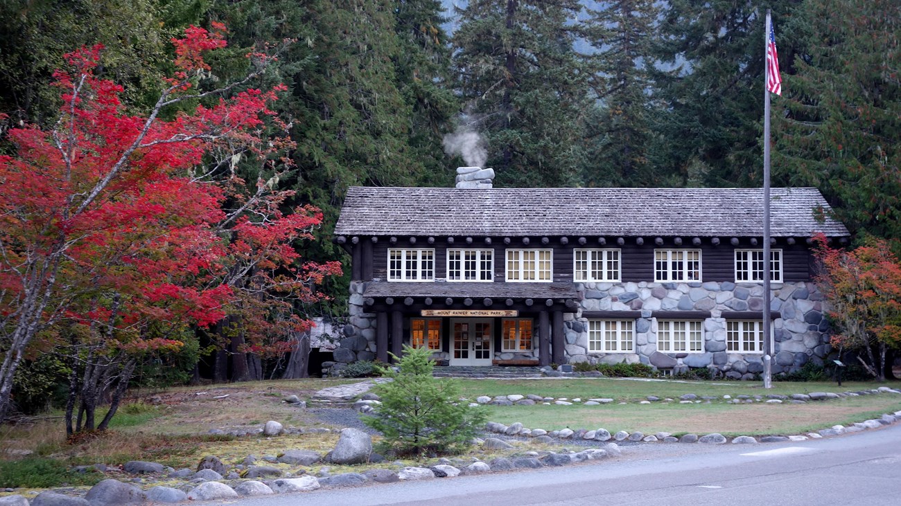A wood and stone historic building framed by conifer trees and vine maples with red foliage.