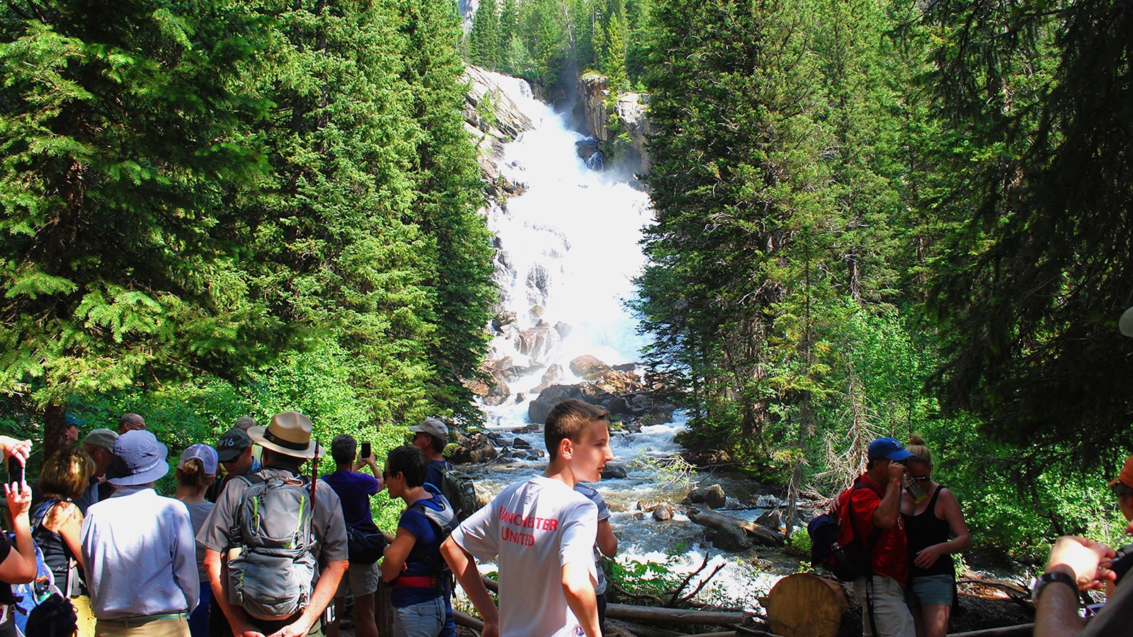 Hidden Falls during the summer with visitors and ranger admiring it.