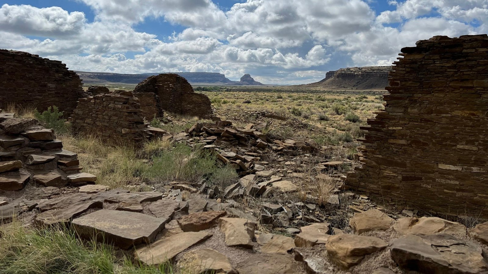 A tall butte is seen in the distance through the remains of old constructed walls at Hungo Pavi, wit