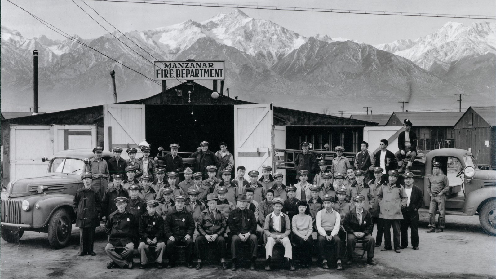 Black and white photo of a group of men in front of building with fire vehicles surrounding
