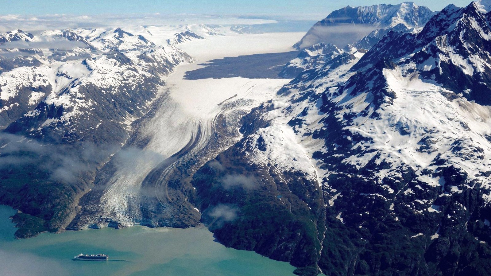 A cruise ship is dwarfed by an expansive sheet of glacial ice.