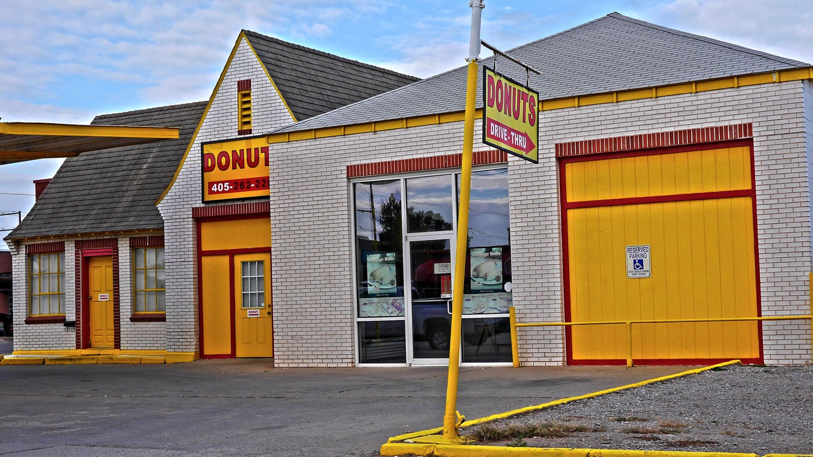 A white building with yellow doors trimmed in red, a steep gabled roof, and sign that reads