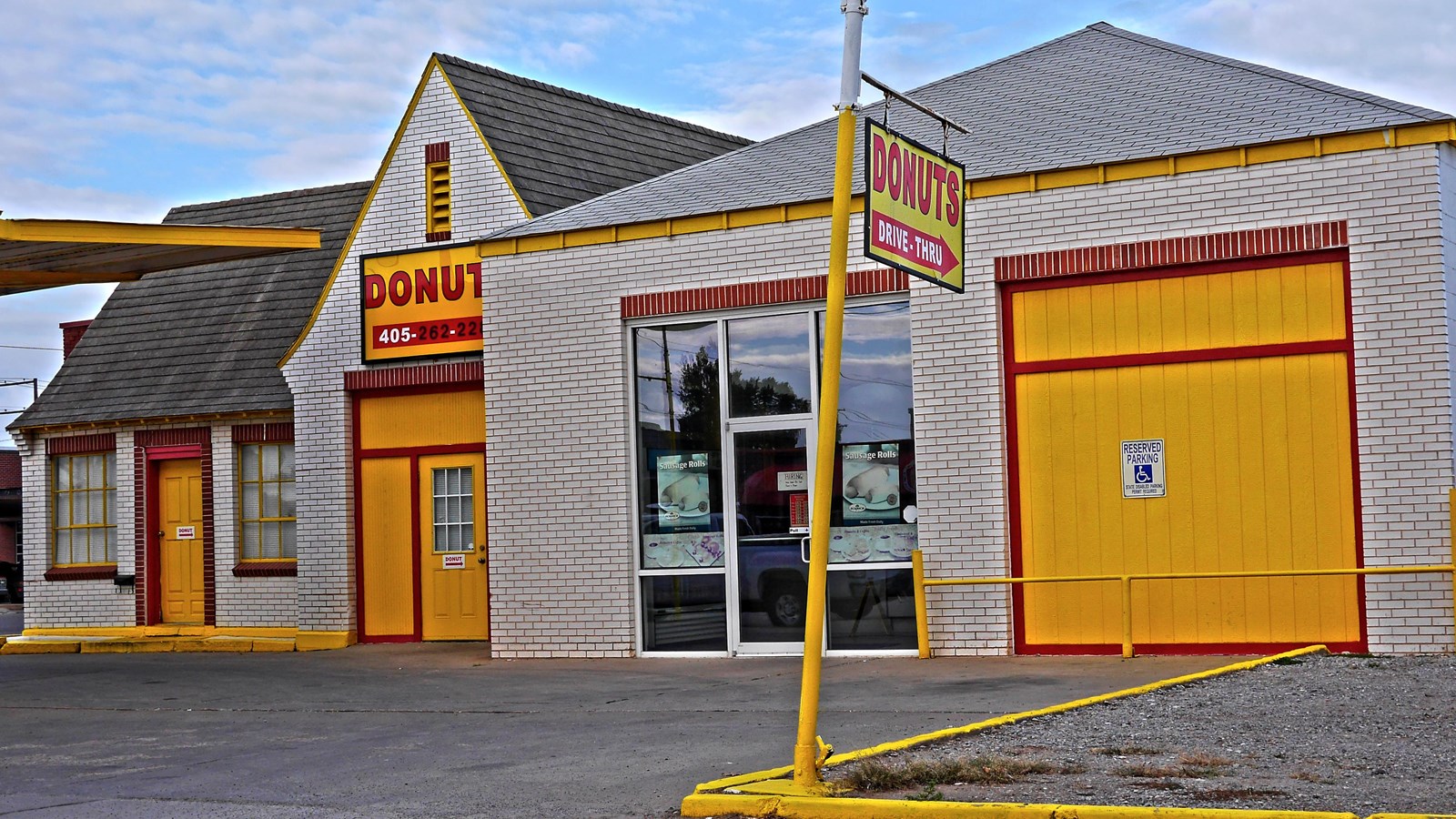 A white building with yellow doors trimmed in red, a steep gabled roof, and sign that reads 