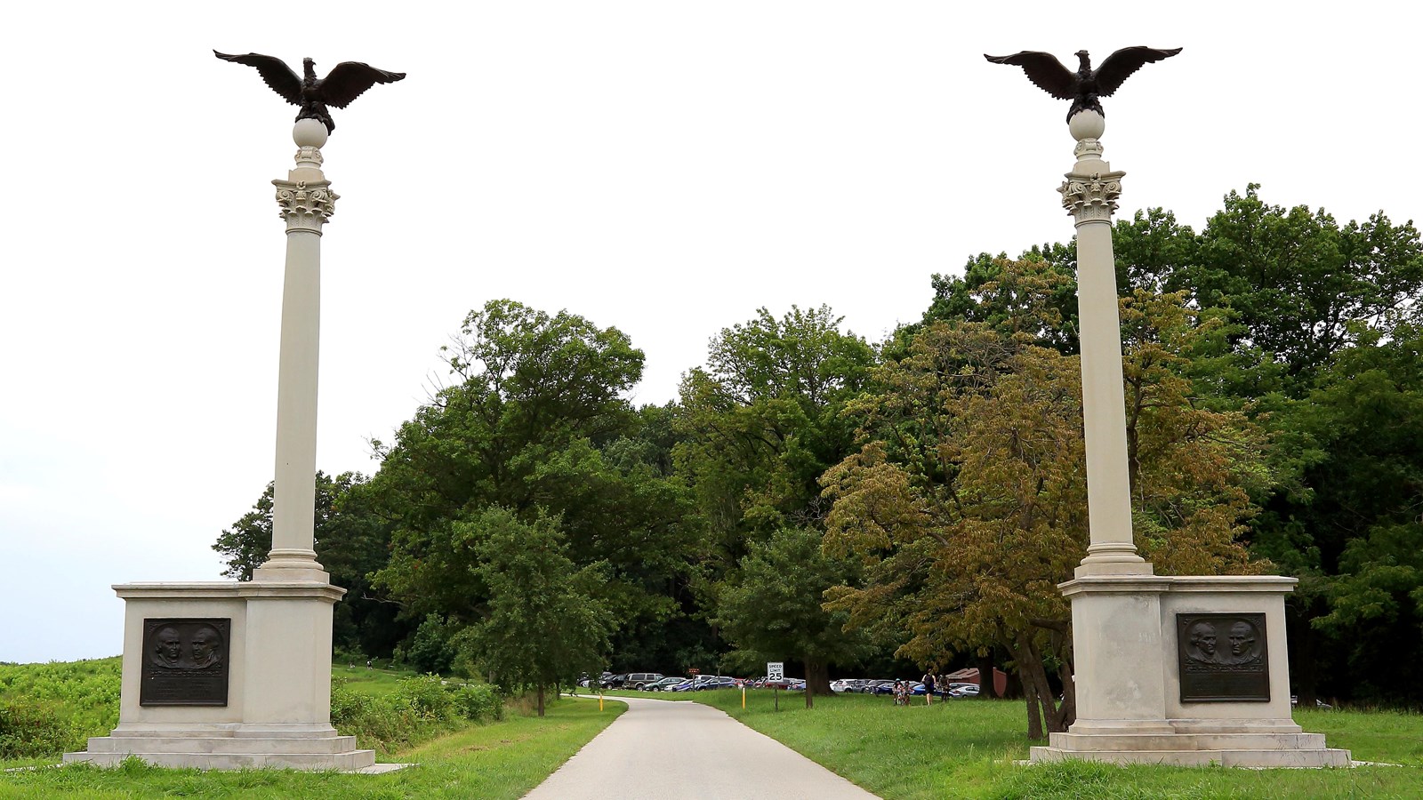 Two columns with bronze eagles on top and bas relief plaques at the bottom flank the road.