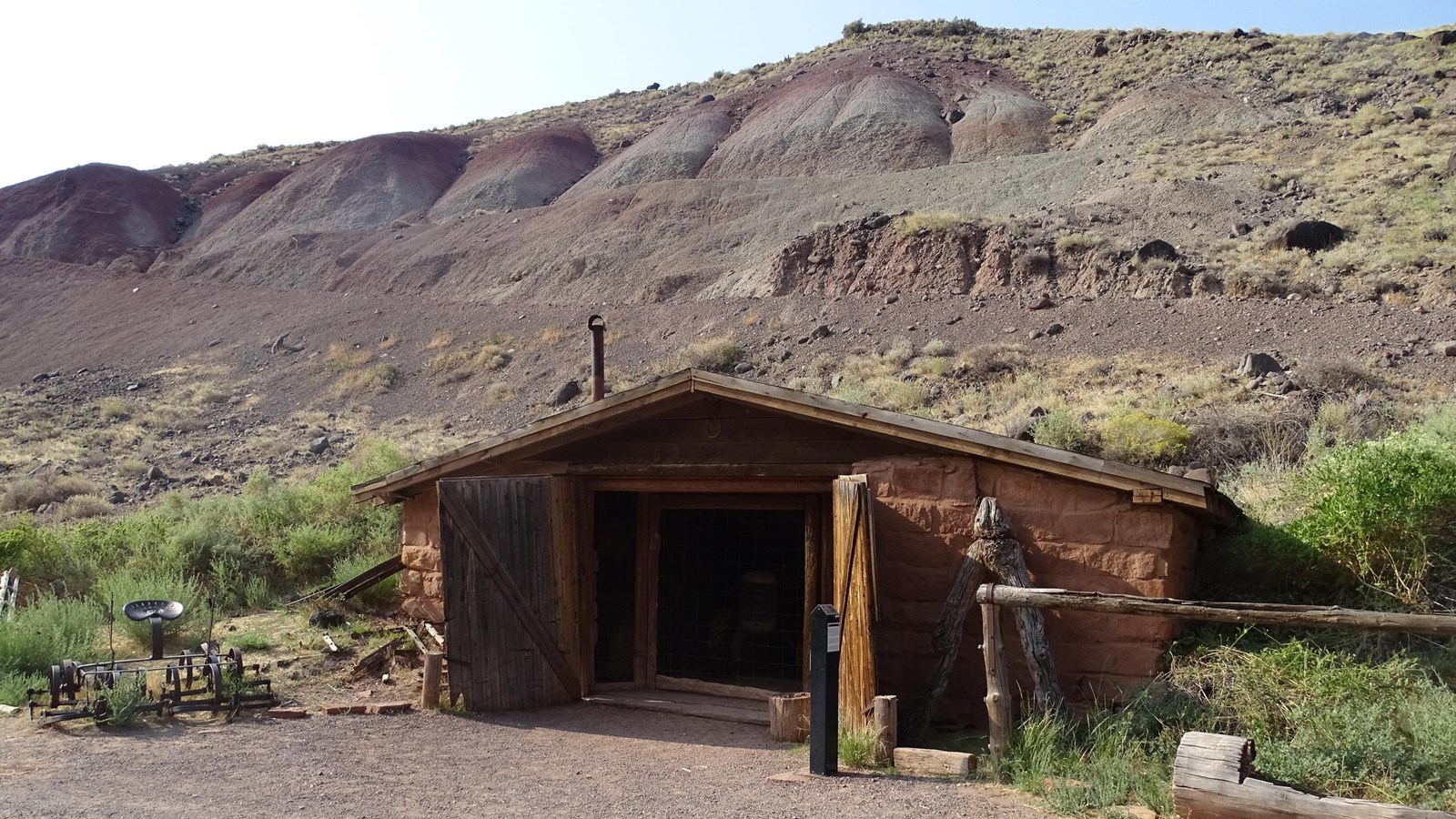 Small Small sandstone building built into gray hillside, with a dirt roof, and open doors.