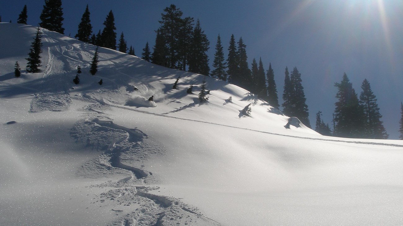 A skier heads downhill on a steep snow-covered slope.