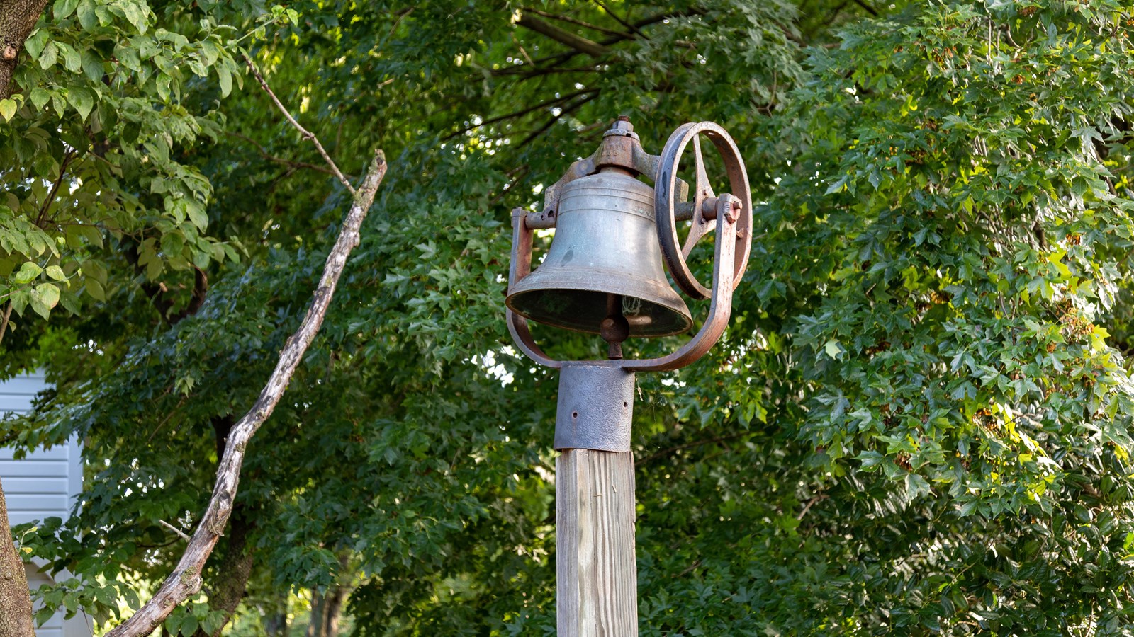 The iron bell farmhouse bell stands on a wood post. A pulley wheel is connected to the side