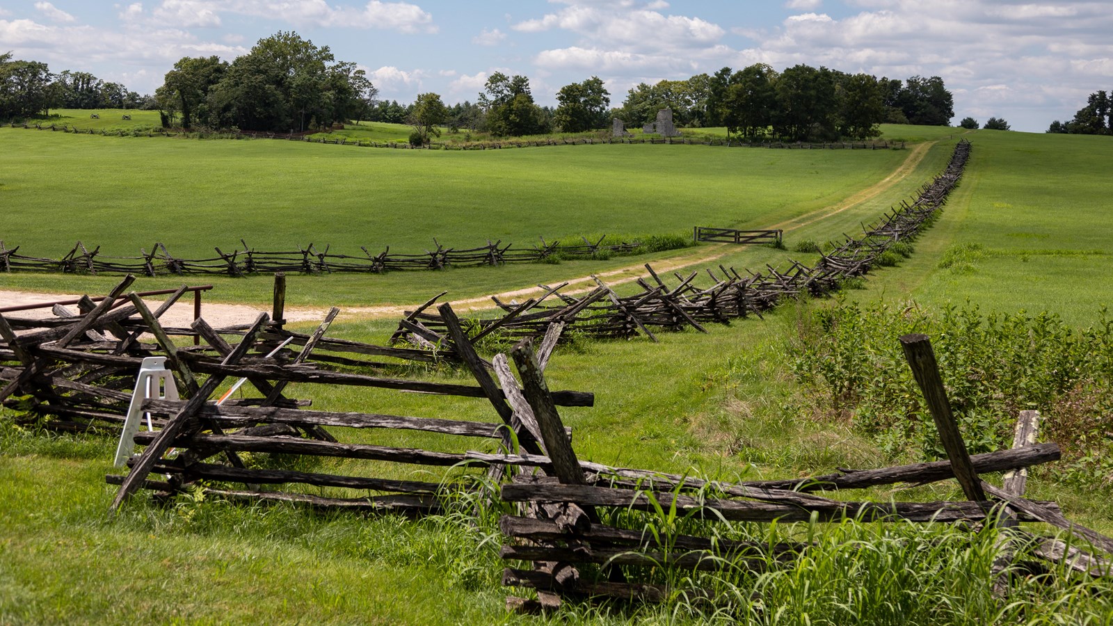 A wooden worm fence lines a dirt road, stretching to the horizon.