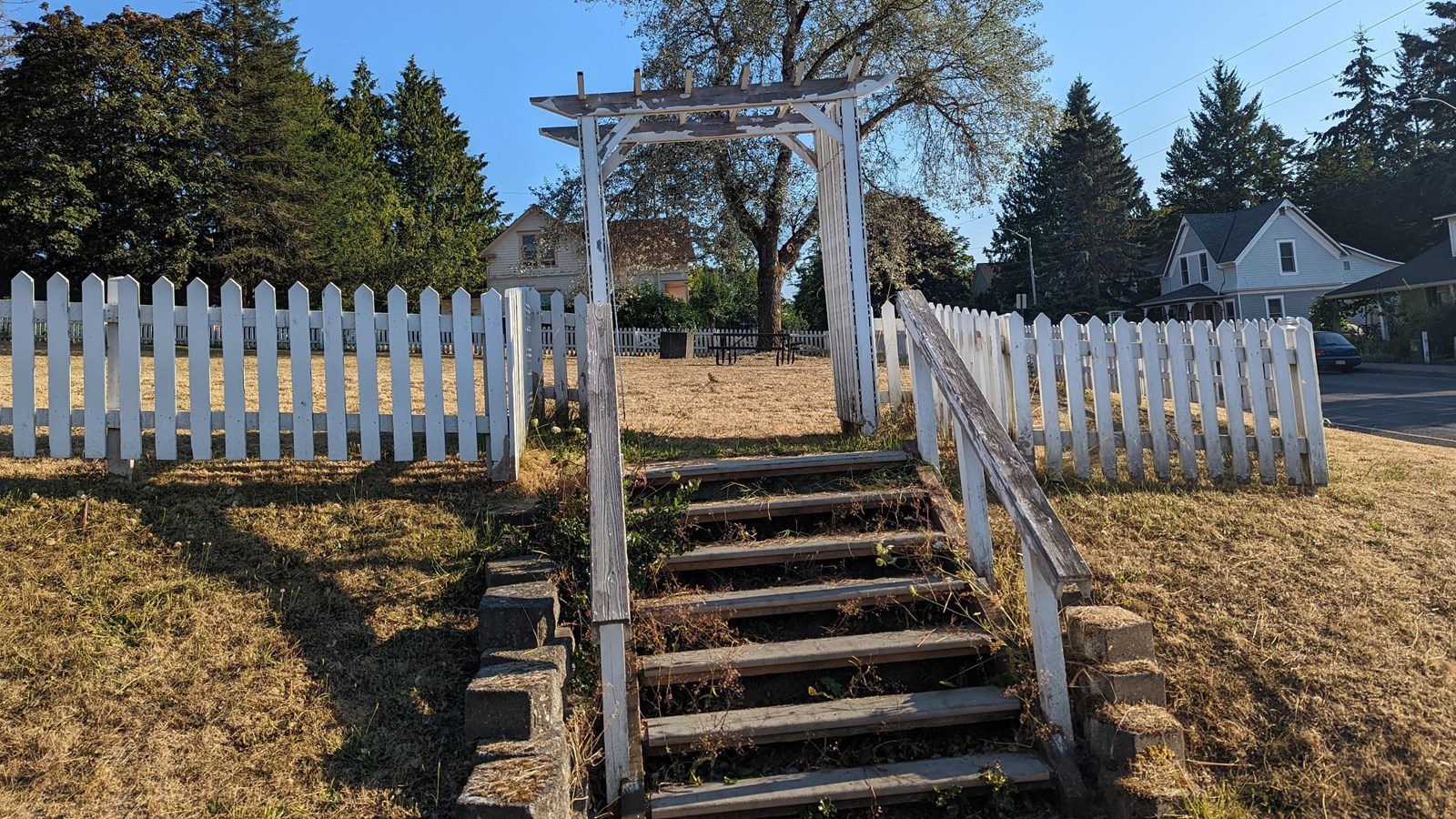 Color photo of a staircase and white picket fence leading to a grassy field