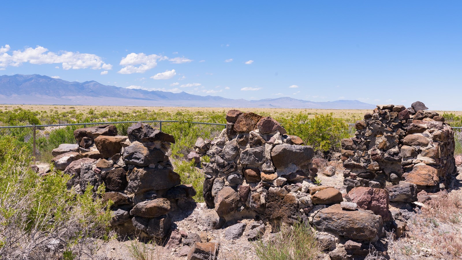 Jagged stone walls rise from a desert plain beneath blue sky and distant mountains.
