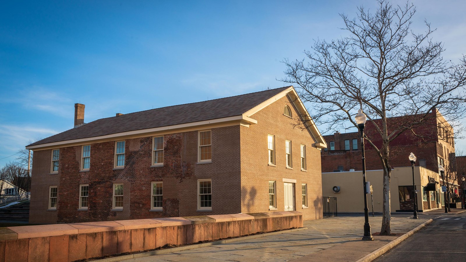 Corner view of a square, two-story, red brick building with white-trimmed windows.