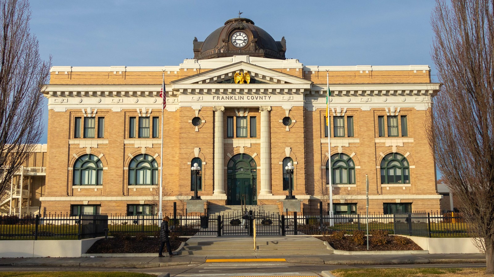 An ornate brick banded building with a central entrance featuring a clock-towered dome and a gold ea